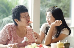 Asian adult daughter feeding fruit to senior mother